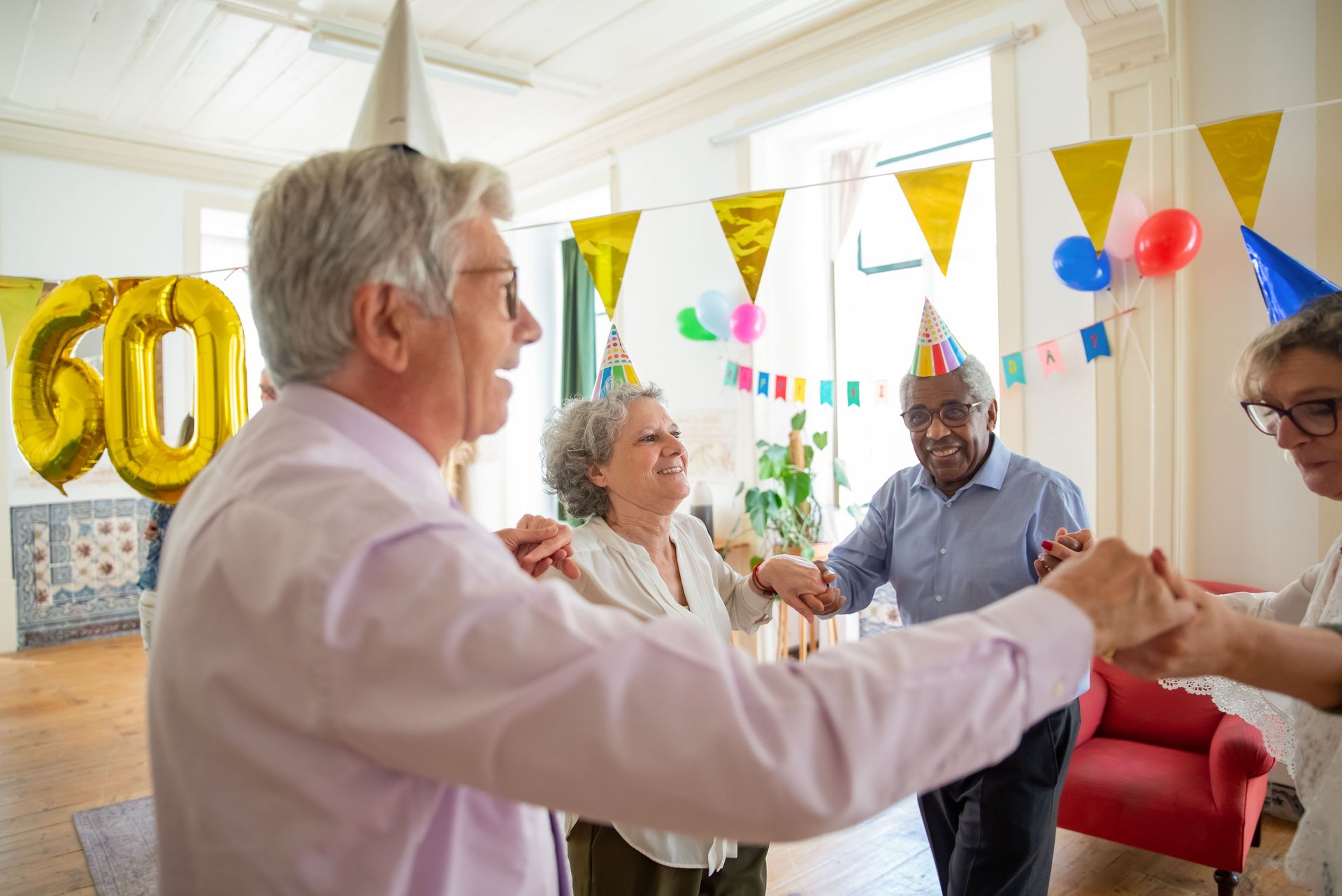 Group of seniors celebrating a birthday indoors with party hats and decorations.